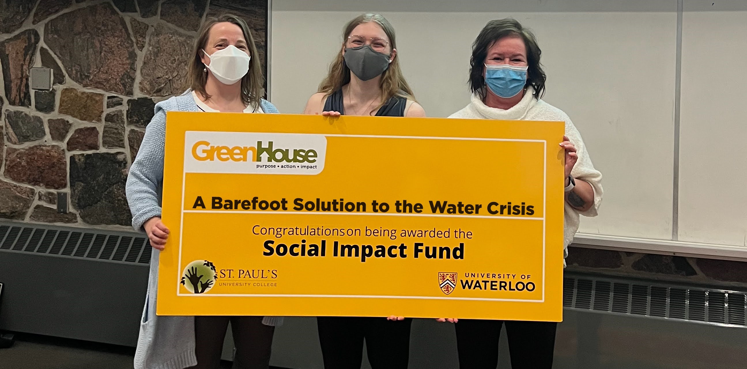 Three women holding a large yellow sign saying "A Barefoot Solution To The Water Crisis - Congratulations being awarded The Social Impact Fund